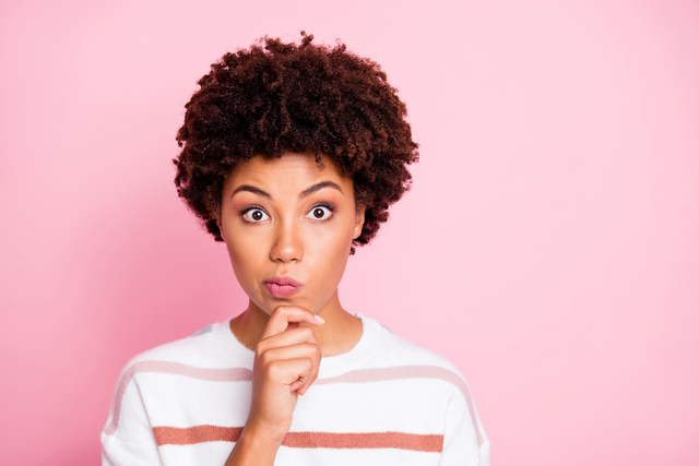 Photo of amazed misunderstanding cute funny black woman touching, her chin lost deeply in thoughts wearing white striped sweated isolated over pink pastel color background
